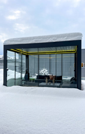 Pergolux Pergola mit Glaswänden im Winter, bedeckt mit Schnee und beleuchtetem Innenraum.
