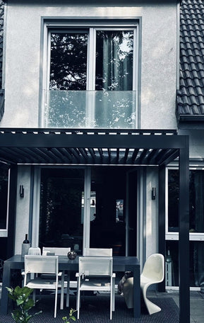 Anthrazitfarbene Pergolux Pergola als Terrassenüberdachung an einem Einfamilienhaus mit Essbereich und Grill.