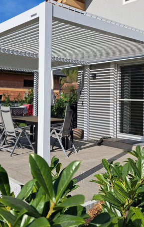 Weiße Pergolux Pergola auf einer Terrasse mit Esstisch und Gartenstühlen im Sonnenschein.