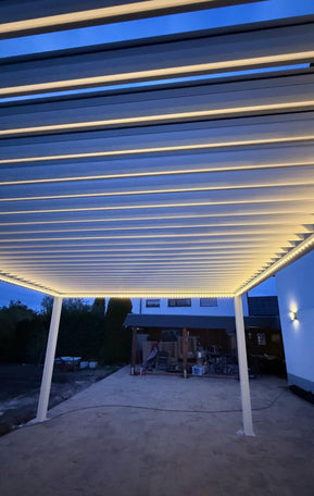 Pergolux Pergola mit LED-Beleuchtung an einem Haus, aufgenommen bei Dämmerung.