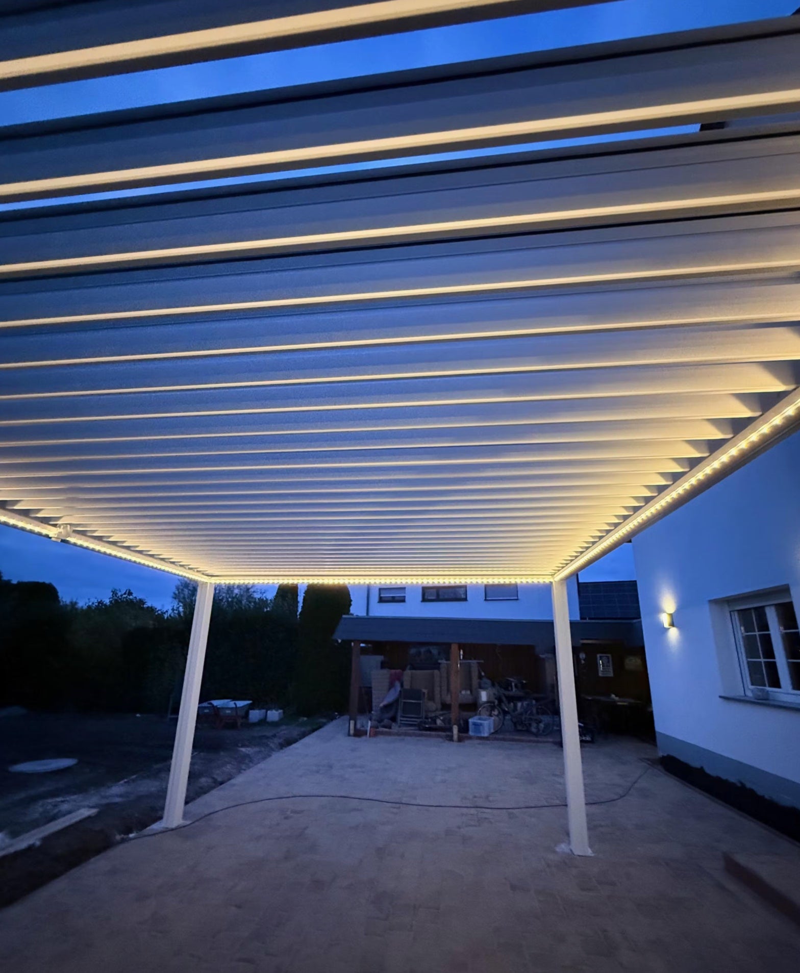 Pergolux Pergola mit LED-Beleuchtung an einem Haus, aufgenommen bei Dämmerung.
